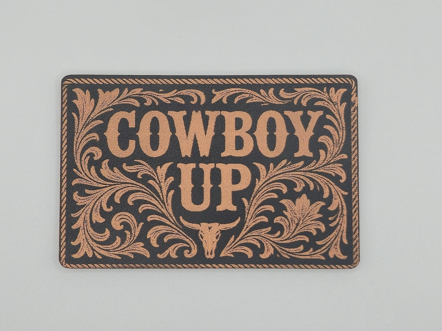 Decorative hat patch with 'Cowboy Up' text and decorative border on a black background.