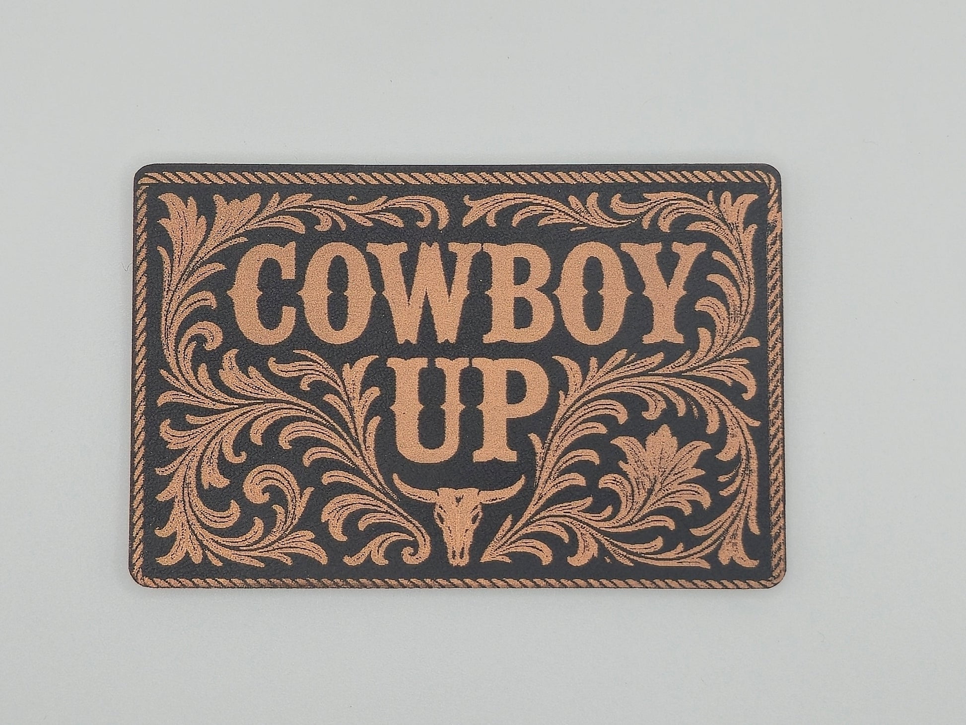 Decorative hat patch with 'Cowboy Up' text and decorative border on a black background.