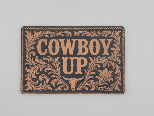 Decorative hat patch with 'Cowboy Up' text and decorative border on a black background.