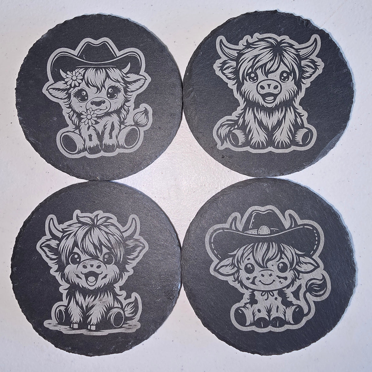 4 slate coasters with various designs of highland cows.